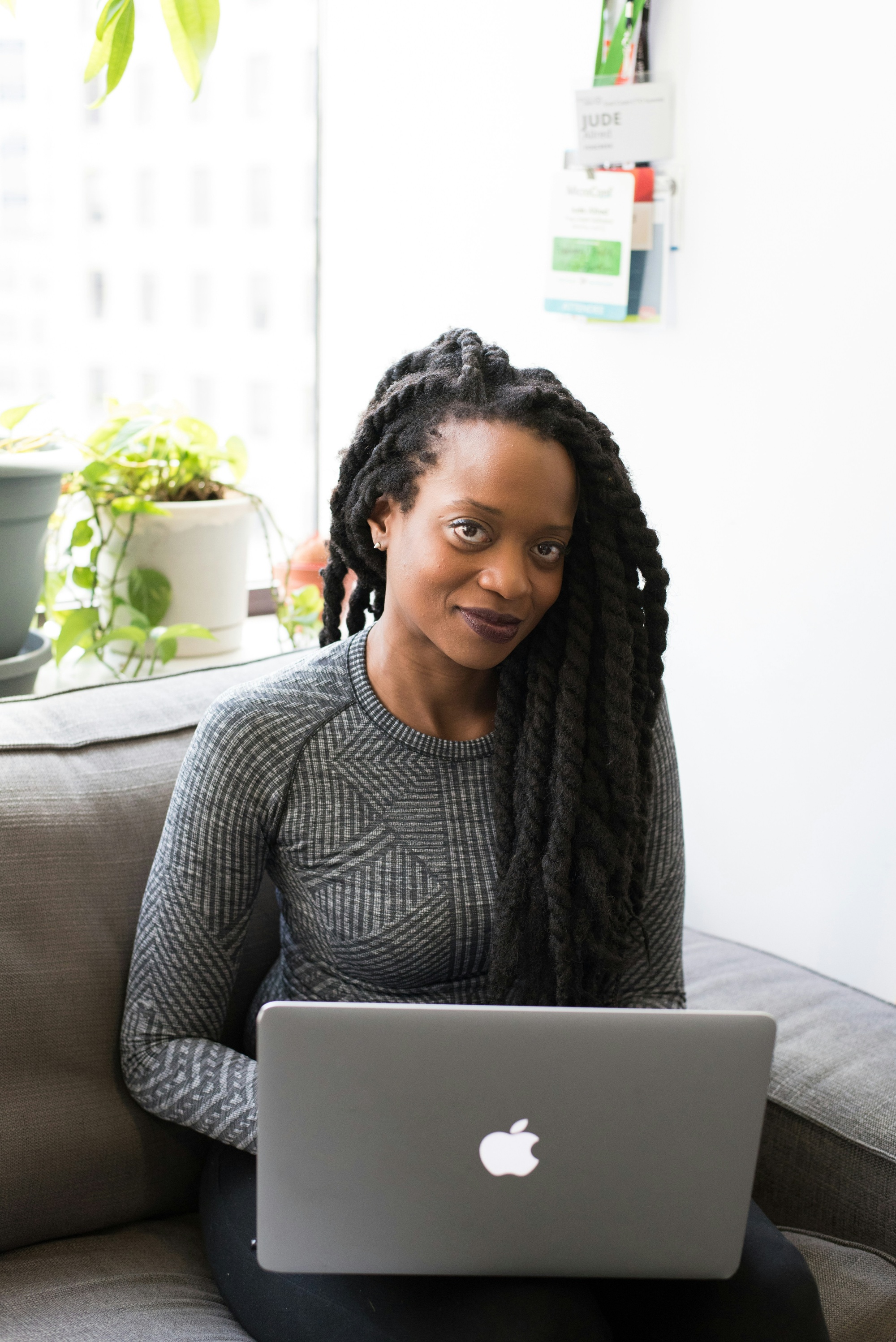 Woman with dreadlocks working on a laptop on a couch